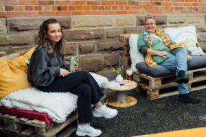 Zwei lächelnde Frauen, die auf gemütlich geposlterten Paletten sitzen