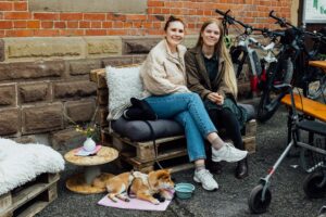 Zwei lächelnde Frauen auf einer Palette sitzend mit einem Hund.