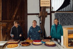 Lachende Landfrauen, die hinter einer Kuchentheke stehen für den Verkauf davon.