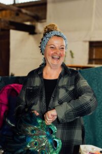 Lächelnde Standbetreiberin, die eine venezianische Pfauenmaske in der Hand hält.